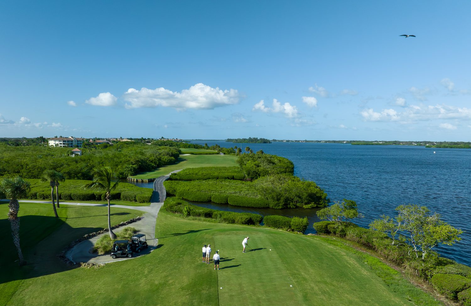 Oceanside golf hole bordering the Indian River Lagoon in Vero Beach, with golfers on the tee and an osprey overhead