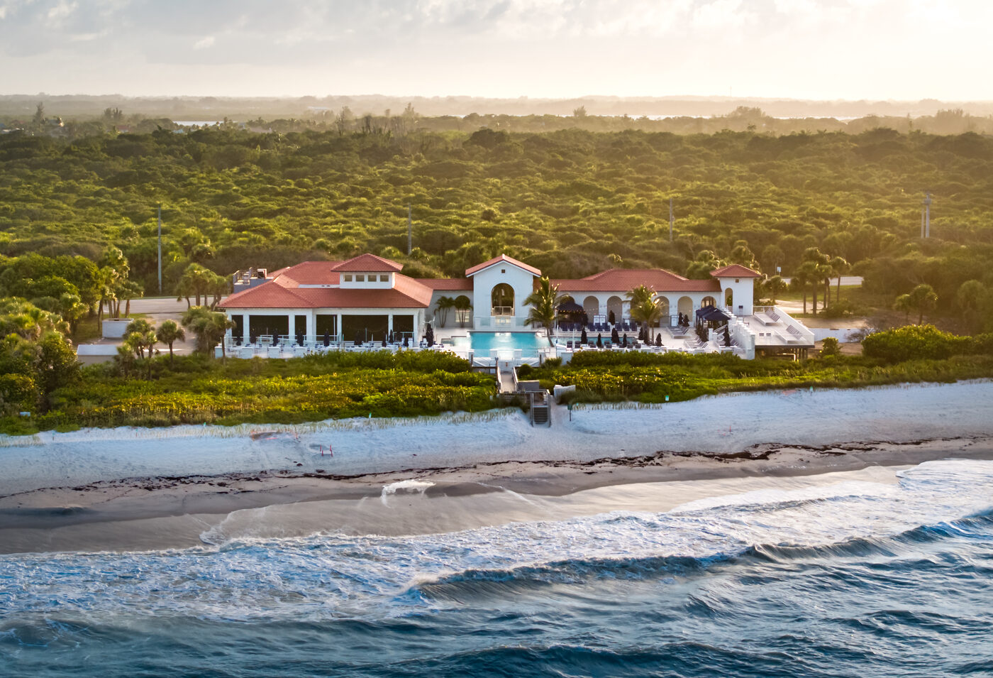 Oceanfront clubhouse at golden hour on the Vero Beach barrier island, waves breaking in the foreground